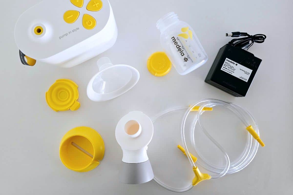 Medela breast pump replacement parts including tubing, connectors, bottles, membranes, and accessories beside a Medela Pump In Style breast pump.